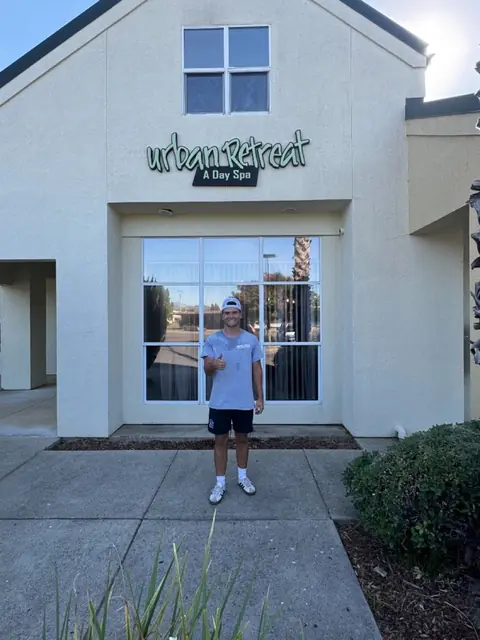 A crew member giving a thumbs up in front of a day spa's large front window