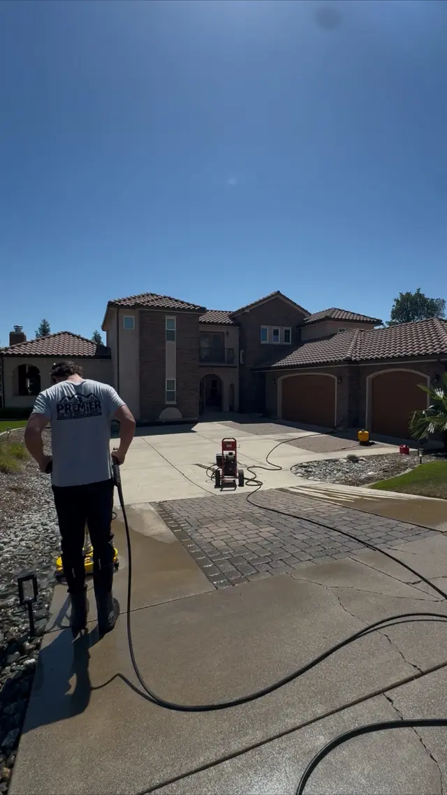 A Premier Exterior crew member pressure washing a long concrete driveway