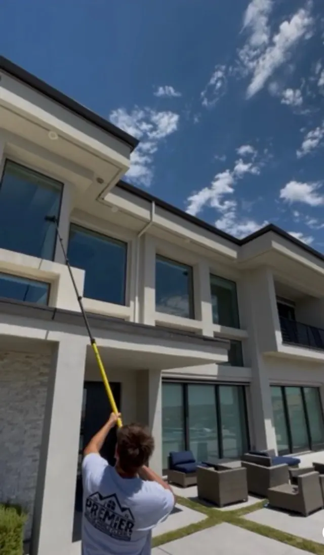 A Premier Exterior crew member washing second-story windows with a long pole
