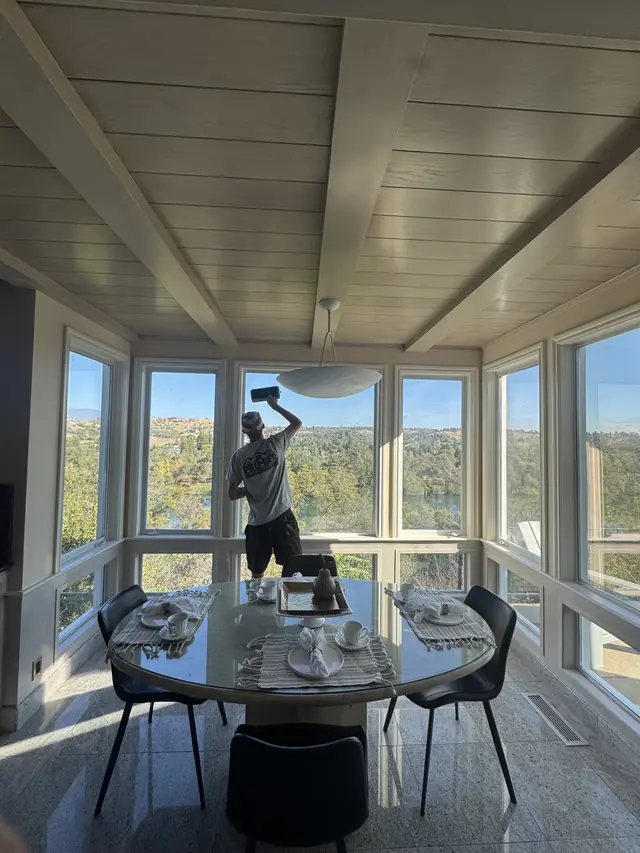 A Premier Exterior crew member cleaning tall inside windows that look out over a river valley