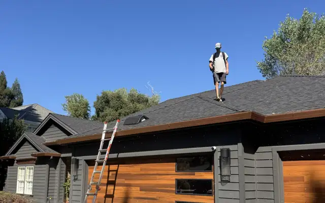 A Premier Exterior crew member on the roof of a home, ladder up at the gutter line