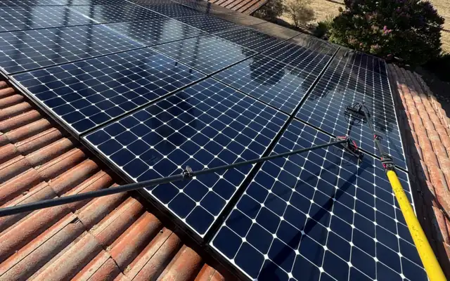 Cleaning a rooftop solar array with a water-fed brush on a long pole