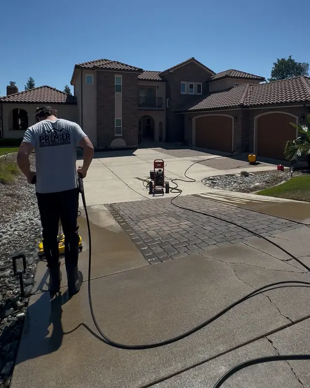 A crew member running a surface cleaner across a long concrete driveway