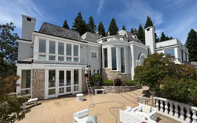 A Premier Exterior crew member on a ladder washing the painted walls at the back of a large two-story home