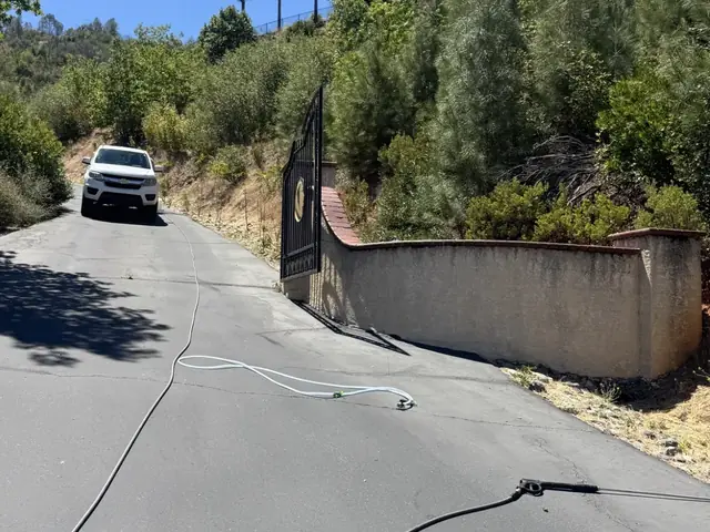 Painted entry walls beside a gated driveway, streaked dark before washing, with our hoses laid out on the drive