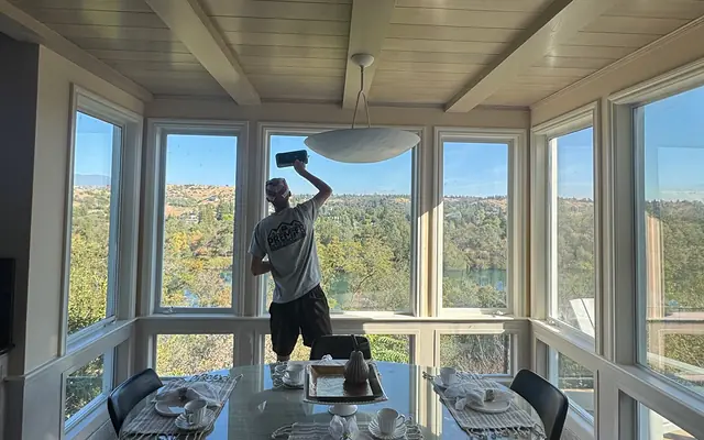 A Premier Exterior crew member cleaning the inside of a sunroom window that looks out over a river valley