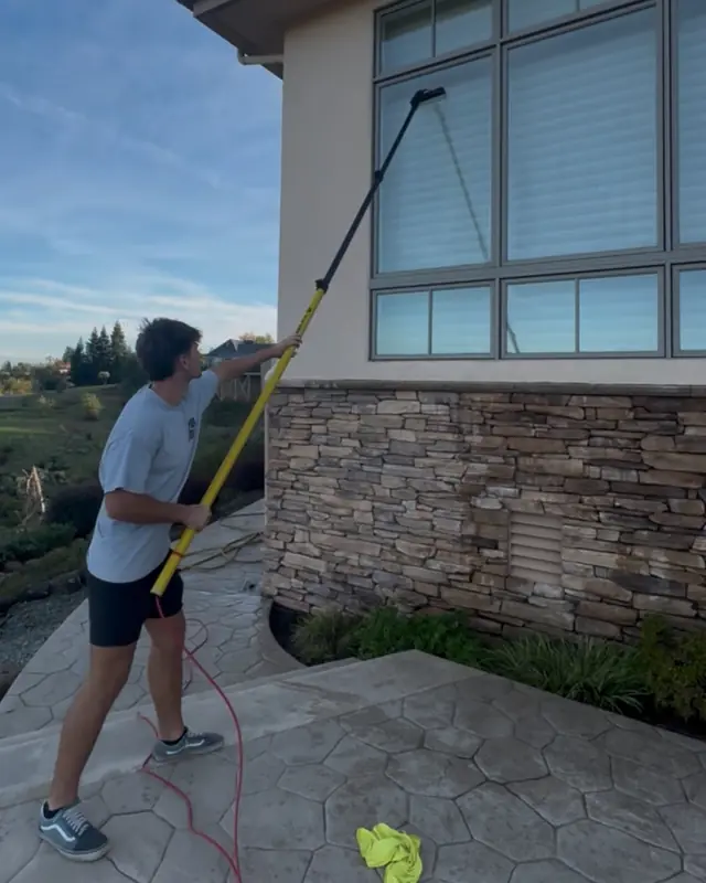 A crew member on a stamped-concrete patio washing tall windows with a long water-fed pole