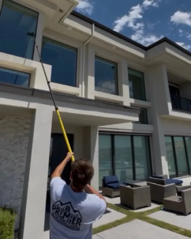A Premier Exterior crew member washing second-story windows from the patio with a long pole