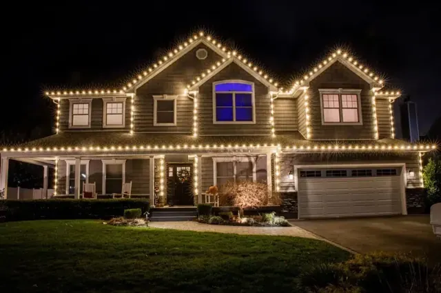 A two-story home with warm white lights on the rooflines, corners and porch columns