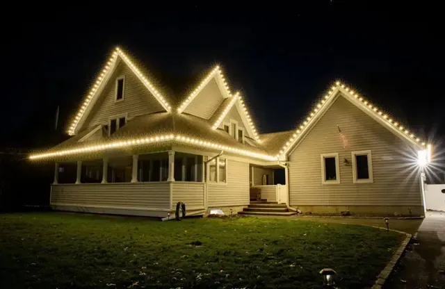A farmhouse with warm white lights tracing every peak of the roofline