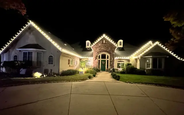 A single-story home at night with warm white lights along the rooflines and gables